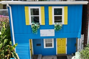 Edificio de dos pisos con fachada azul, contraventanas amarillas y un letrero que dice 'Blue Bungalow'.