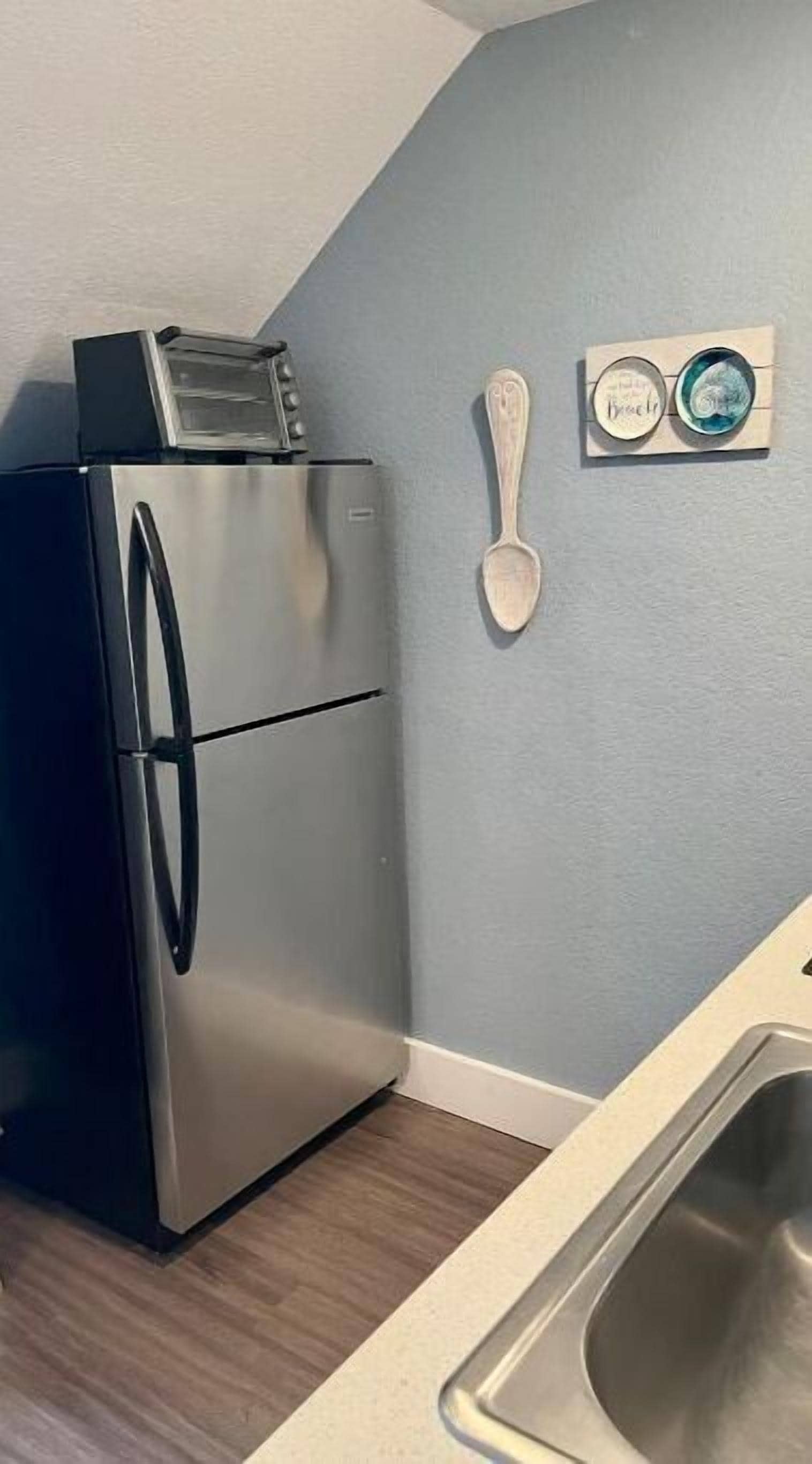 A kitchen with a stainless steel refrigerator, a wooden spoon, and a small decorative item on the wall.