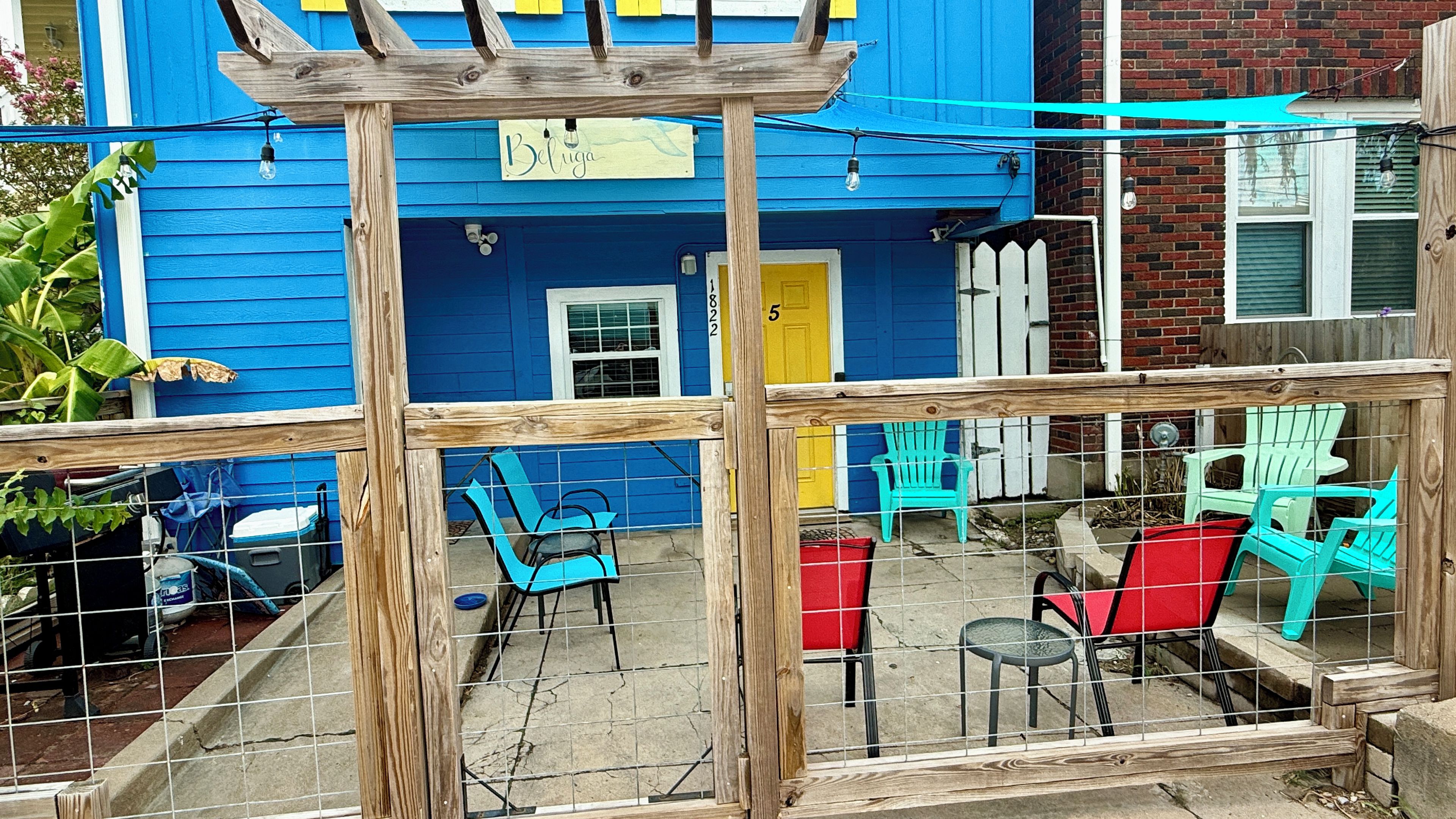 Una casa azul con una pérgola de madera, un letrero que dice 'Belinda' y sillas de exterior.