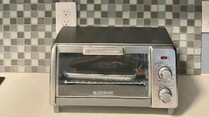 Een keuken met een toaster op het aanrecht, een betegelde spatwand en planken met verschillende borden.