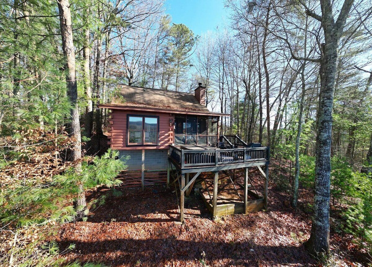 A cabin with a wooden deck, surrounded by trees.