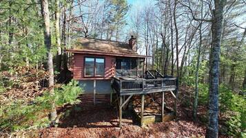 A cabin with a wooden deck, surrounded by trees.