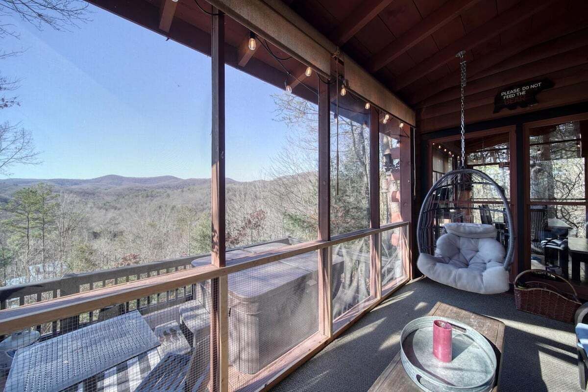 A covered outdoor area with a view of the mountains, a hanging chair, and a table with a candle.