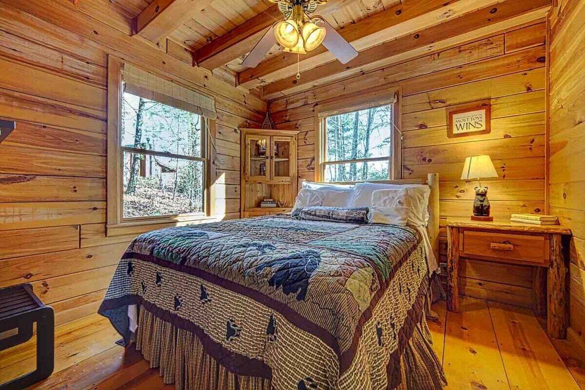 A wooden cabin bedroom with a bed, a nightstand, a cabinet, and a window.