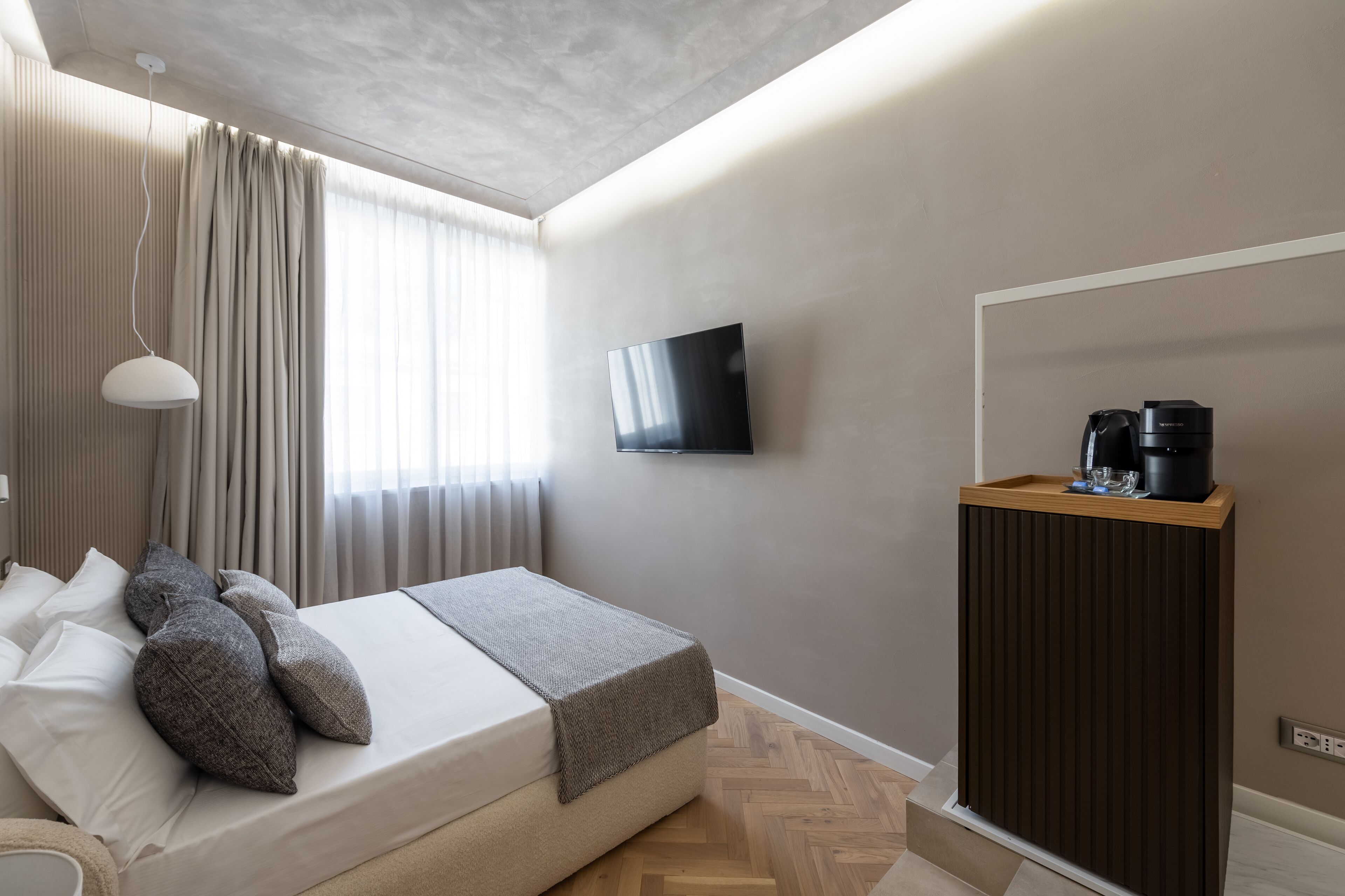 A modern hotel room with a bed, a flat-screen TV, a coffee machine, and a wooden side table.