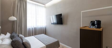 A modern hotel room with a bed, a flat-screen TV, a coffee machine, and a wooden side table.
