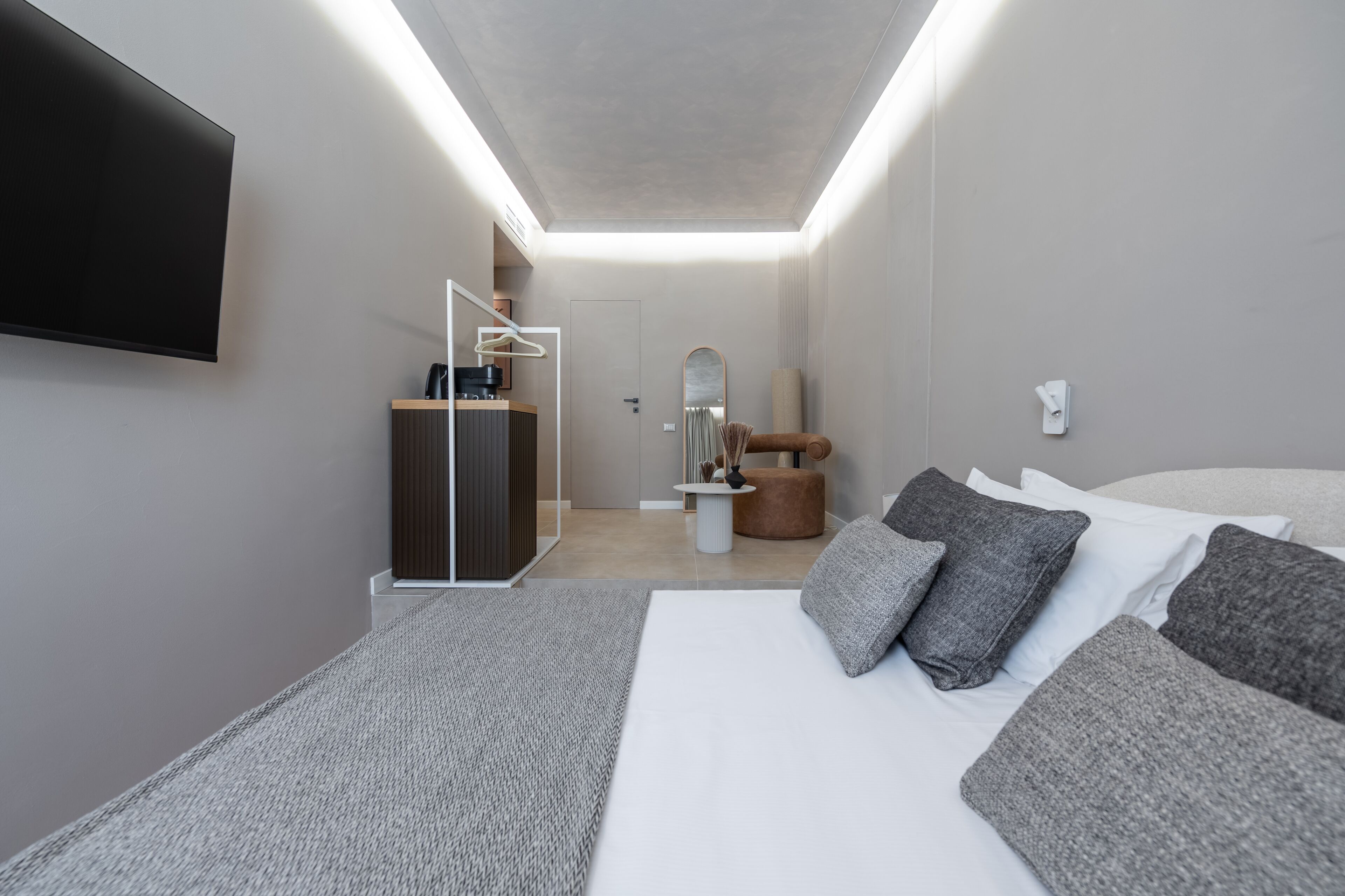 Een moderne hotelkamer met een groot bed, een flatscreen televisie aan de muur, een klein bureau met stoel, een spiegel en een ronde tafel met een vaas.
