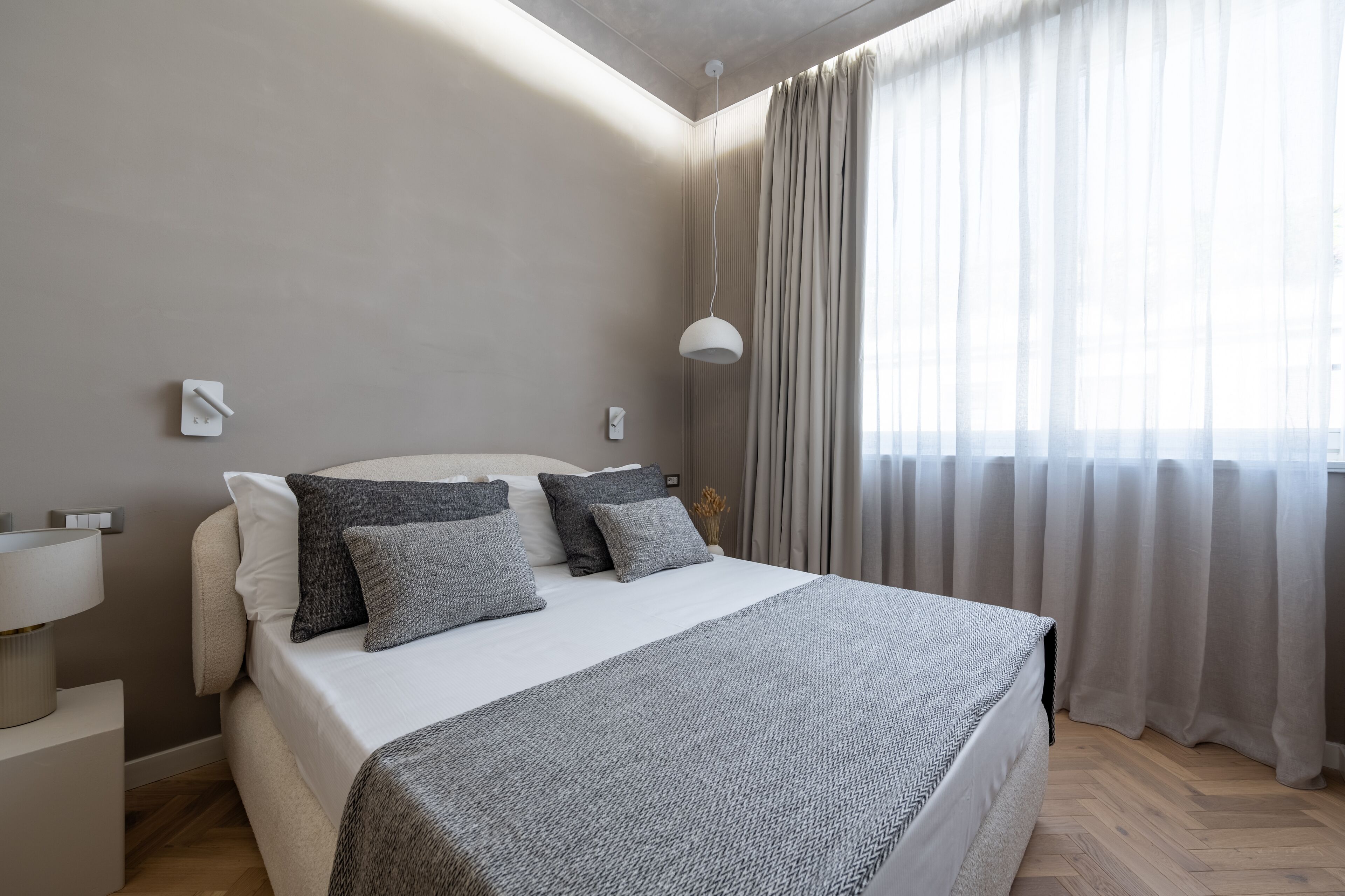 Een moderne slaapkamer met een groot bed, nachtkastjes, een lamp en een raam met gordijnen.