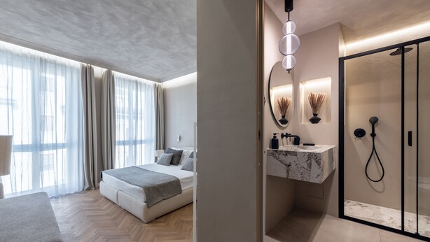 A modern hotel room with a large bed, a wooden herringbone floor, a marble bathroom vanity, and a glass shower enclosure. - Duomo Collection (Milan)