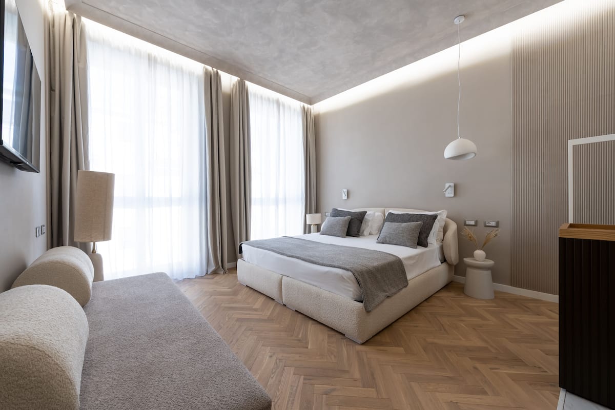 A modern bedroom with a large bed, a bedside table, a lamp, and a view of the outdoors.