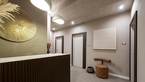 A modern reception area with a wooden reception desk, a large wall-mounted mirror, and a textured wall panel. - Duomo Collection (Milan)