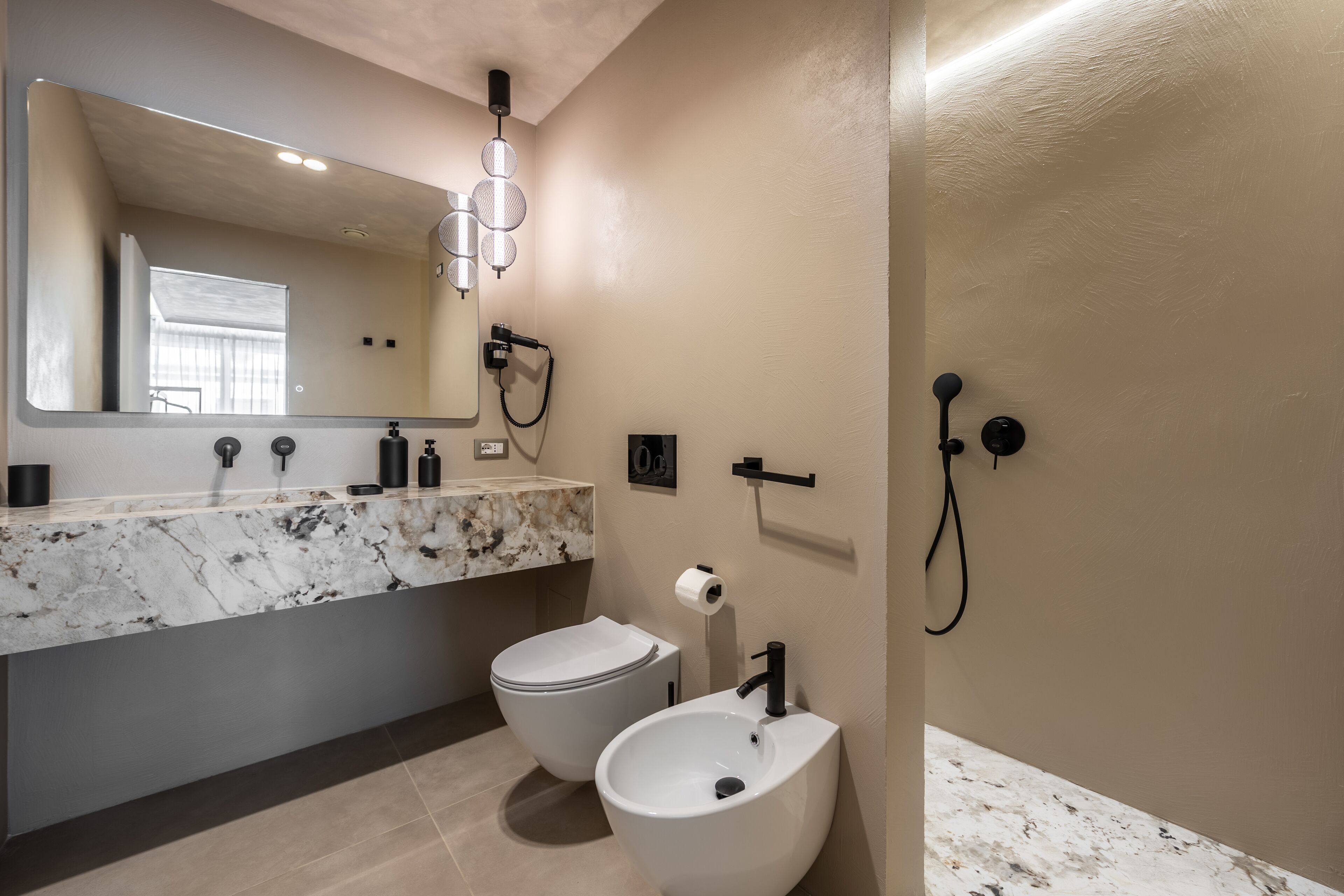 Ein modernes Badezimmer mit Marmorplatte, Toilette, Bidet, großem Spiegel und Dusche.