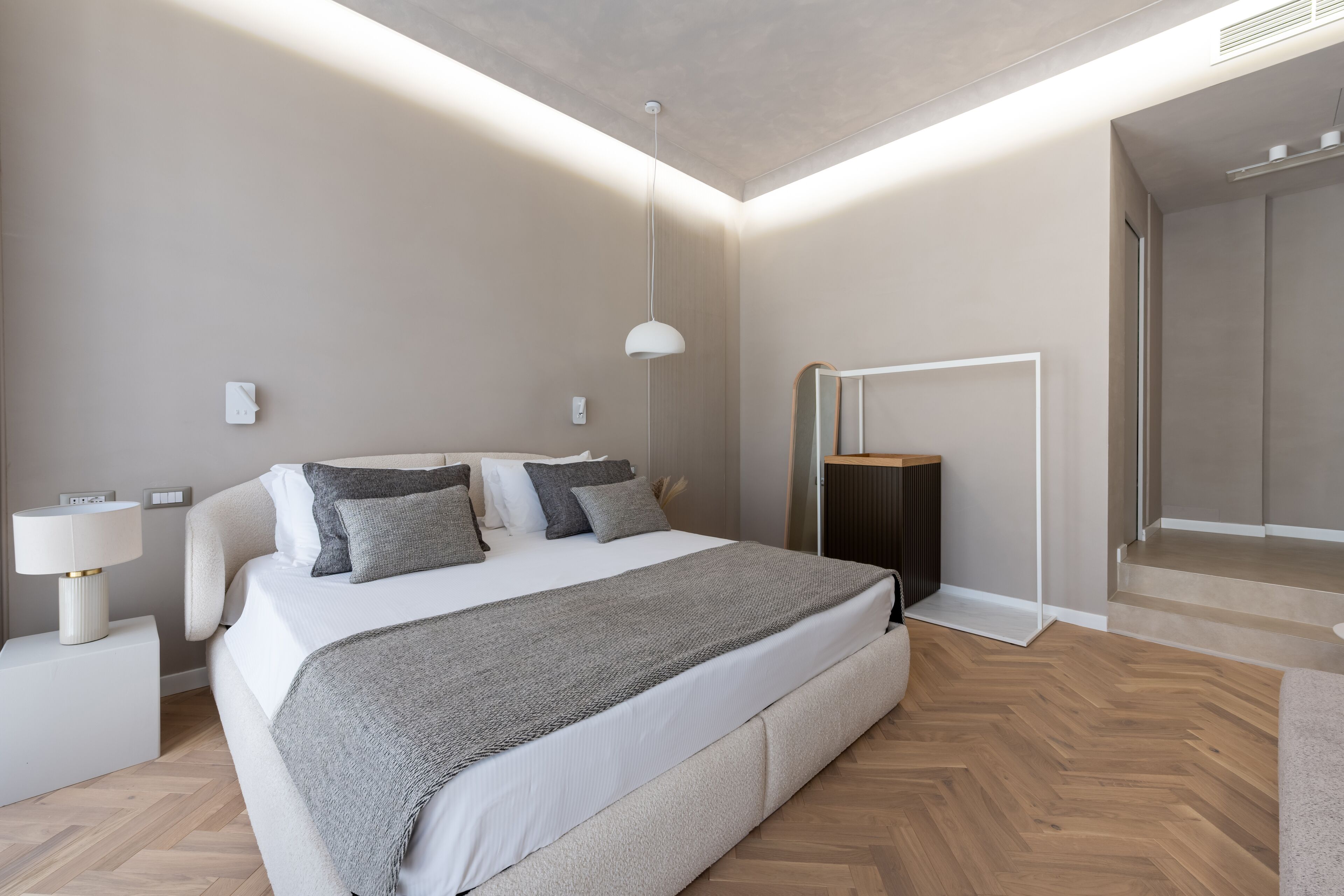 A modern bedroom with a large bed, bedside tables, a mirror, and a ceiling light fixture.