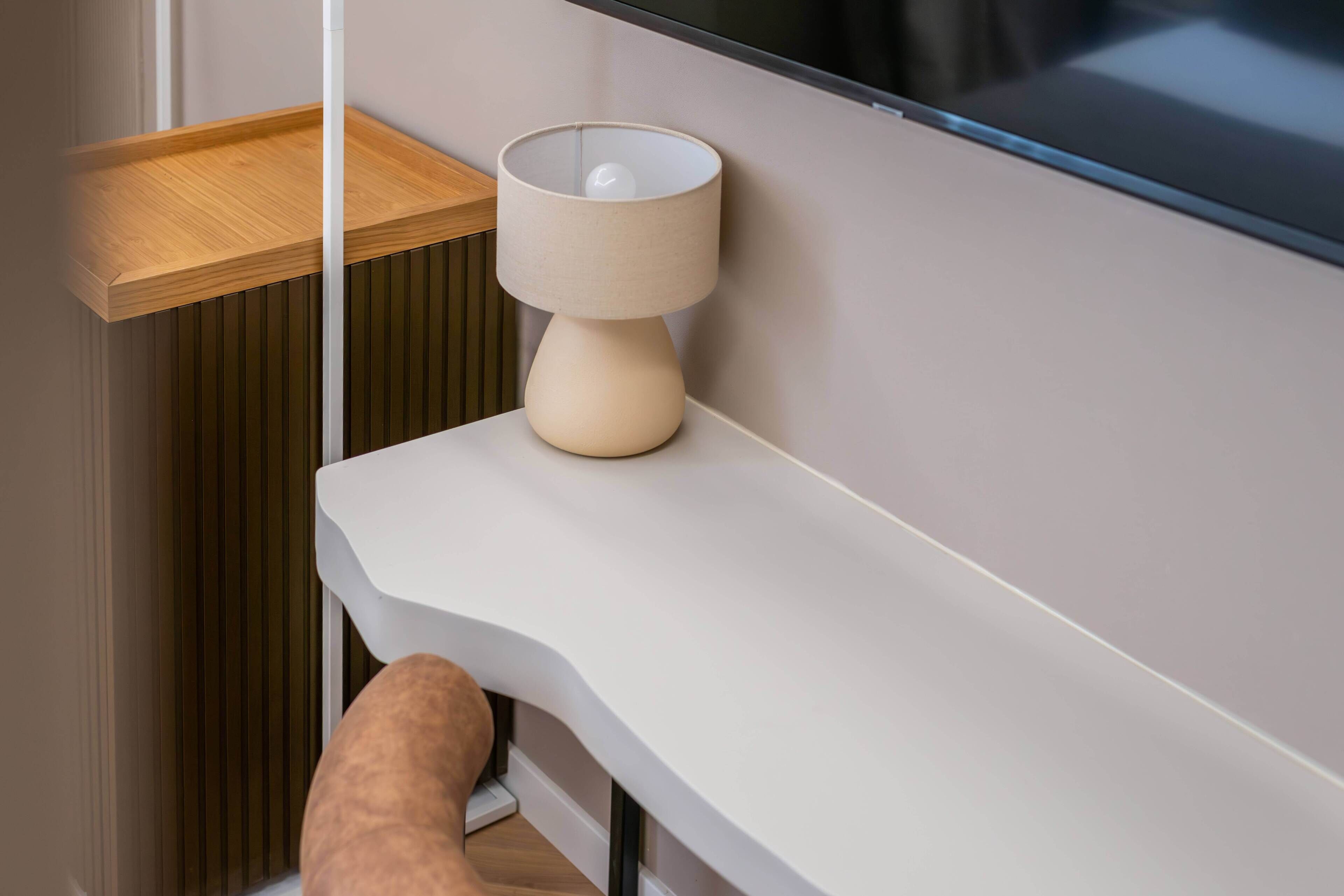 A modern bathroom with a wooden shelf, a white countertop, and a beige lamp.