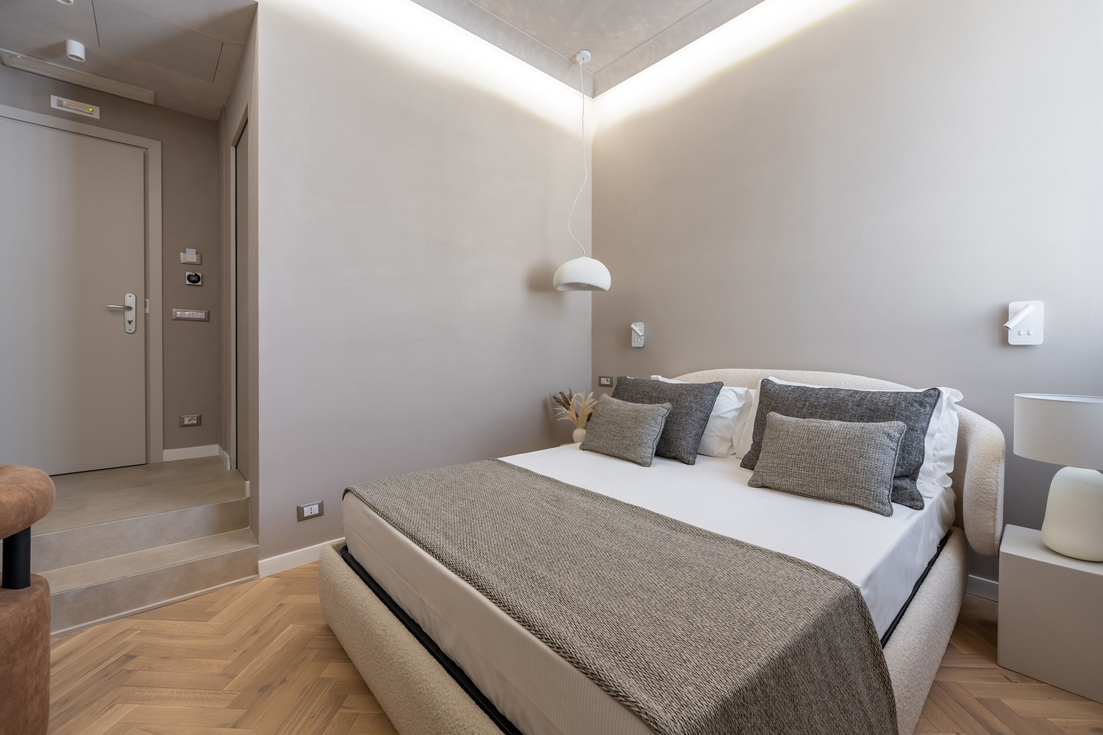 Une chambre moderne avec un grand lit, une table de chevet, une commode et une lampe fixée au mur.