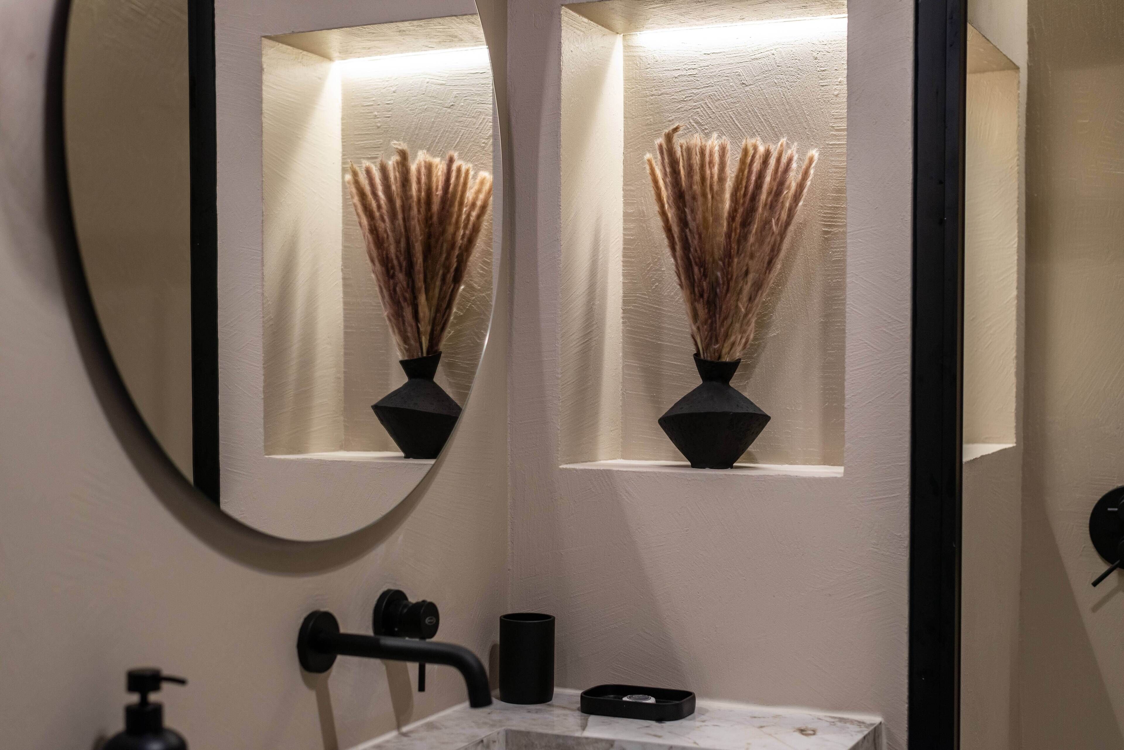 Une salle de bain avec un miroir, un lavabo, un porte-serviettes et un vase contenant des plantes séchées.