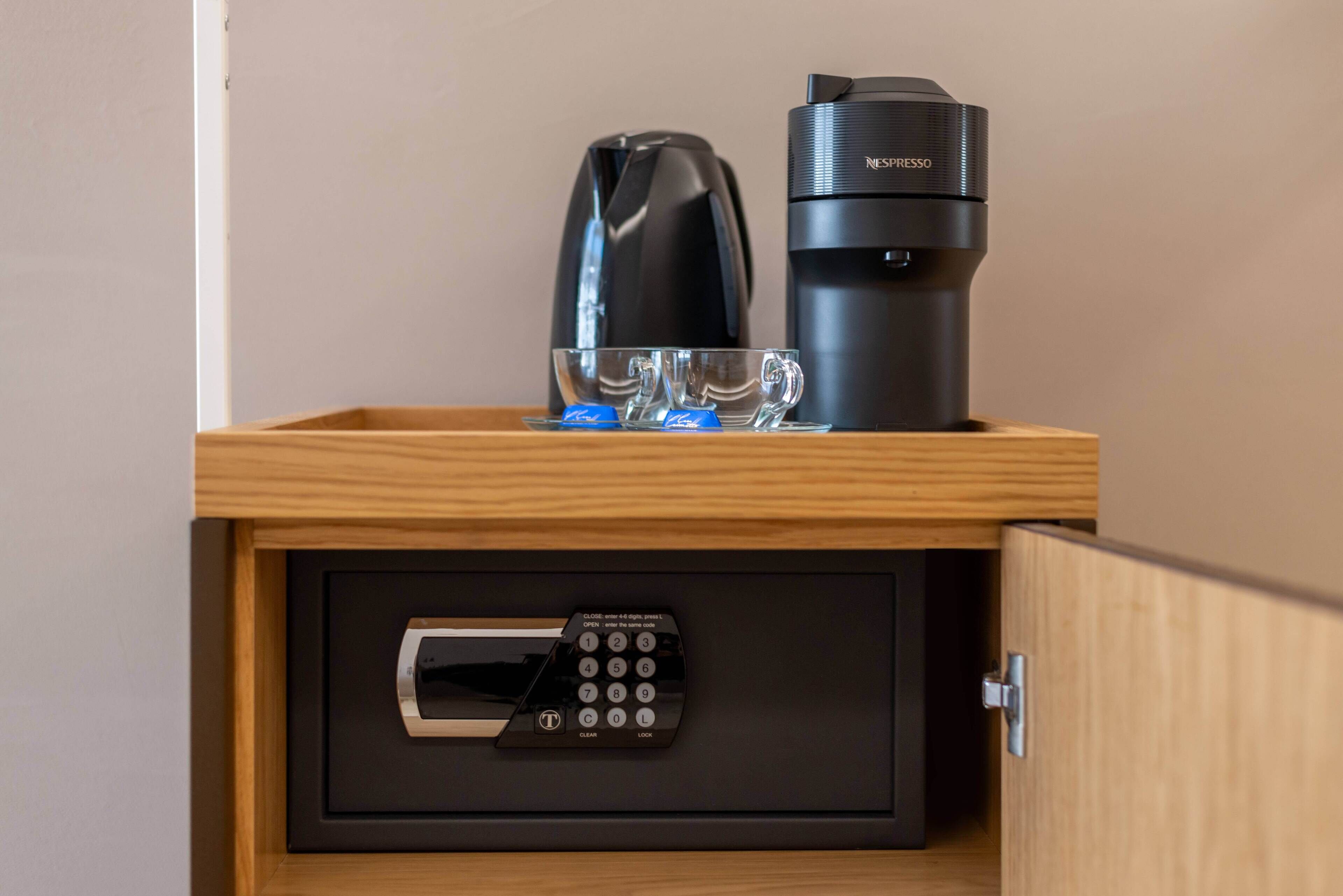 A wooden drawer with a black coffee maker, a black thermos, and a glass mug on top.
