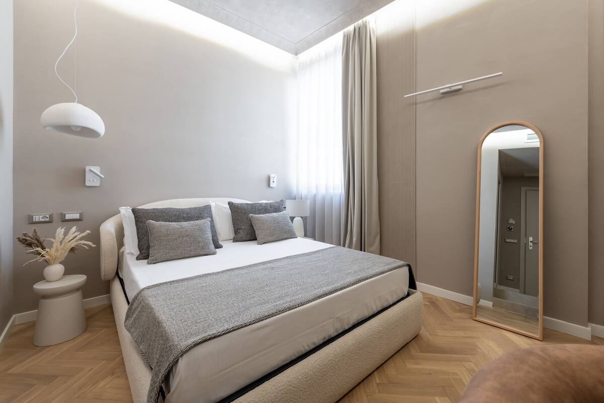 A modern bedroom with a large bed, bedside tables, a mirror, and a ceiling light.