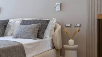 A modern bedroom with a bed, a bedside table with a vase, and a wall-mounted light switch.