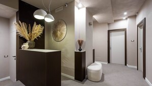 A modern reception area with a wooden reception desk, a vase with pampas grass, a decorative wall piece, and a small white ottoman. - Duomo Collection (Milan)