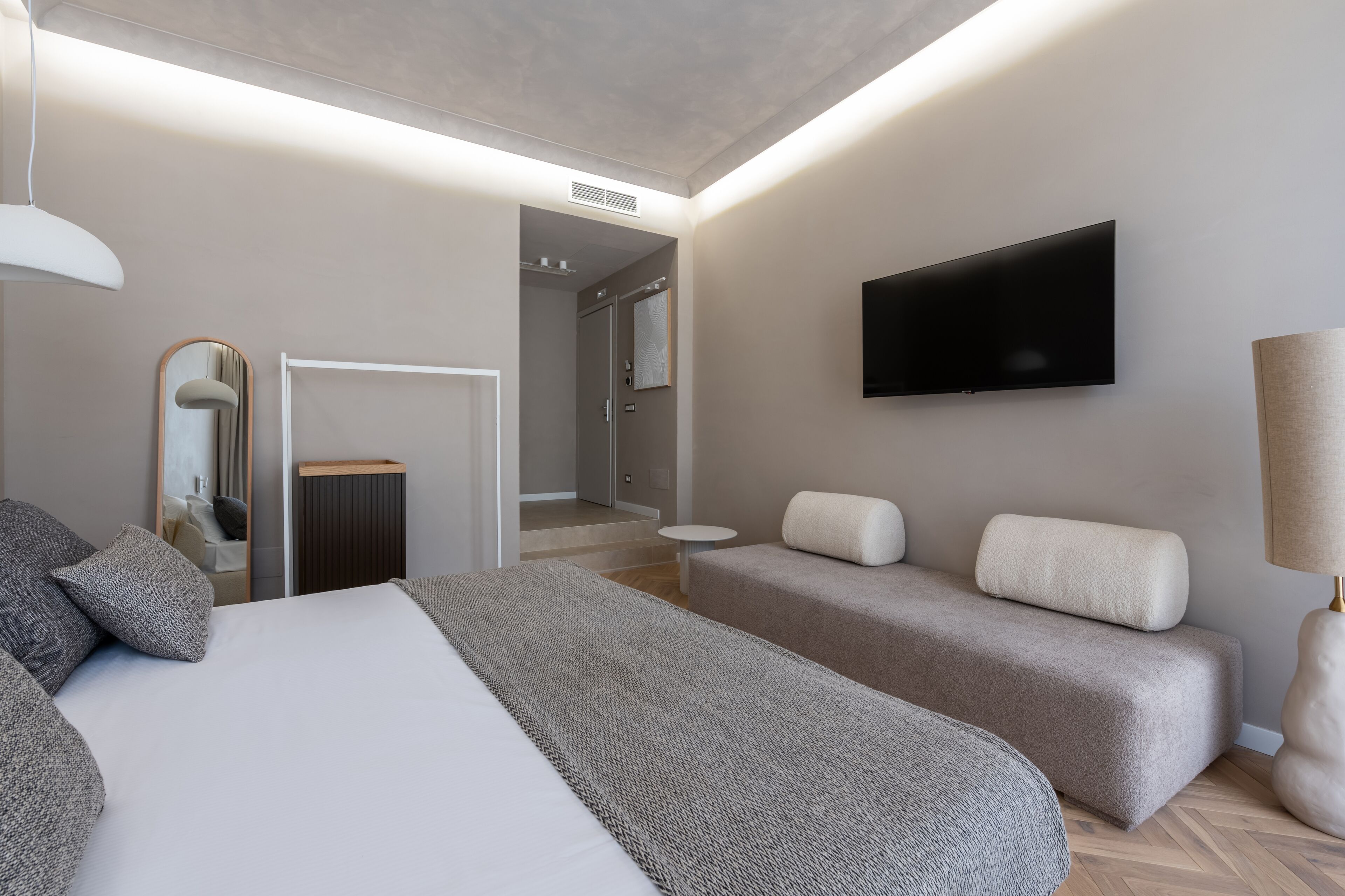 A modern hotel room with a large bed, a sofa, a TV, and a mirror.