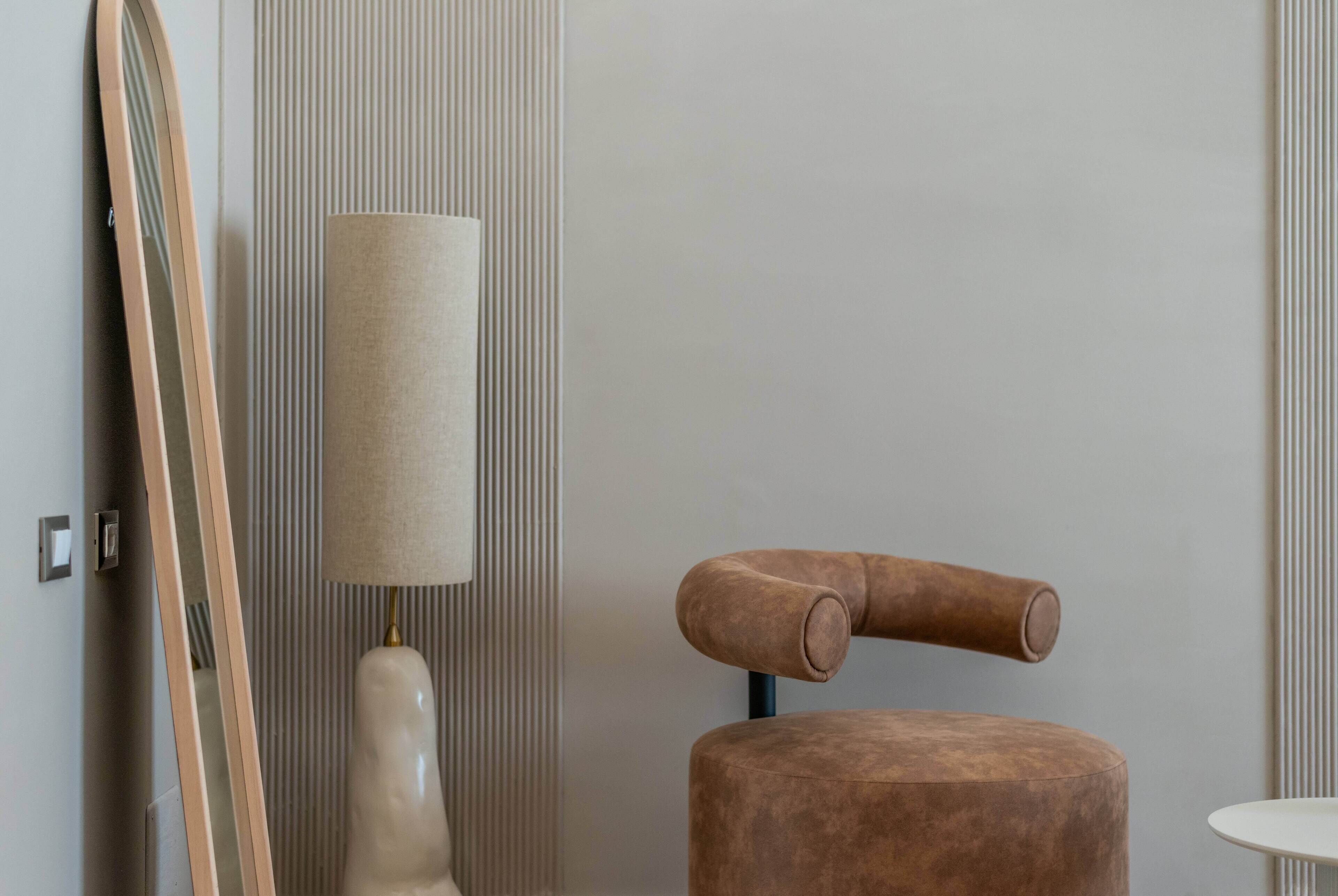 A modern room with a large mirror, a tall lamp, and a unique brown chair.
