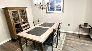 Een eetzaal met een houten tafel en stoelen, een kroonluchter, een kast en een vloerkleed.