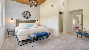 Une chambre à coucher comprenant un lit, des tables de chevet, un banc, un luminaire suspendu et un élément décoratif mural.