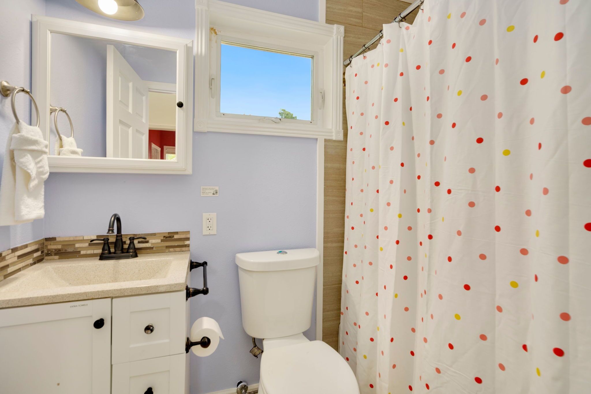 Ein Badezimmer mit Waschbecken, Spiegel, Toilette und einer Duschvorhang mit Punkten.