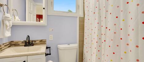 Ein Badezimmer mit Waschbecken, Spiegel, Toilette und einer Duschvorhang mit Punkten.