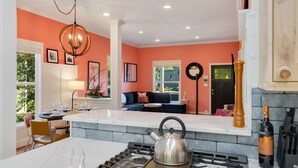 Une cuisine moderne équipée d’une cuisinière à gaz, d’une bouilloire et d’un porte-bouteilles. On y trouve également un coin repas avec une table et des chaises, ainsi qu’un salon avec un canapé et une cheminée.