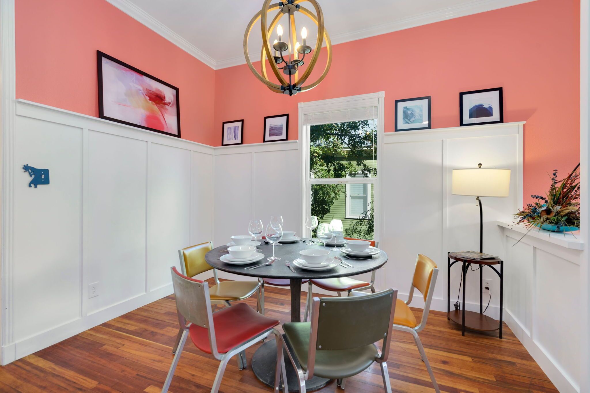 Una sala da pranzo con un tavolo rotondo apparecchiato per sei persone, pareti bianche con pannelli decorativi, un lampadario e opere d'arte incorniciate.