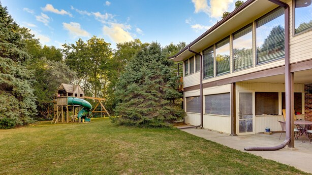 A backyard with a play structure, a house with large windows, and a covered patio area. - Fort Calhoun Home w/ Screened Porch + Playground! (Fort Calhoun)