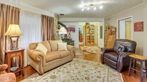 A living room with a brown sofa, a leather armchair, a wooden side table, and a patterned rug. - Fort Calhoun Home w/ Screened Porch + Playground! (Fort Calhoun)