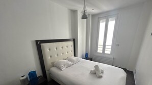 Una cama bien hecha con sábanas blancas, un cabecero y una toalla enrollada encima.