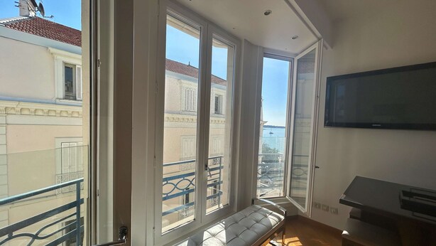 Un balcón con una banca, ventanas amplias y un televisor en la pared.
