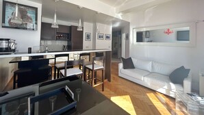 Una cocina moderna con comedor, un sofá blanco y un televisor montado en la pared.