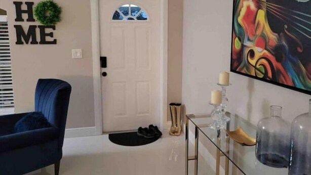 A living room with a blue armchair, a white door with a wreath, a glass coffee table, and a colorful abstract painting. - Beautiful Relaxed Sebring Home. (Sebring)