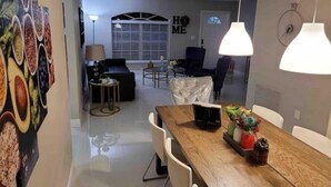 A modern living room with a dining area, featuring a wooden table, white chairs, and a large painting on the wall. - Beautiful Relaxed Sebring Home. (Sebring)