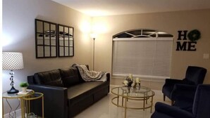 A living room with a black sofa, a glass coffee table, a floor lamp, and a dark blue armchair. - Beautiful Relaxed Sebring Home. (Sebring)