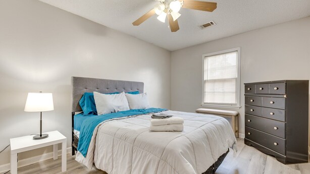 Une chambre à coucher comprenant un lit, une commode, une table de chevet, une lampe et un ventilateur de plafond.