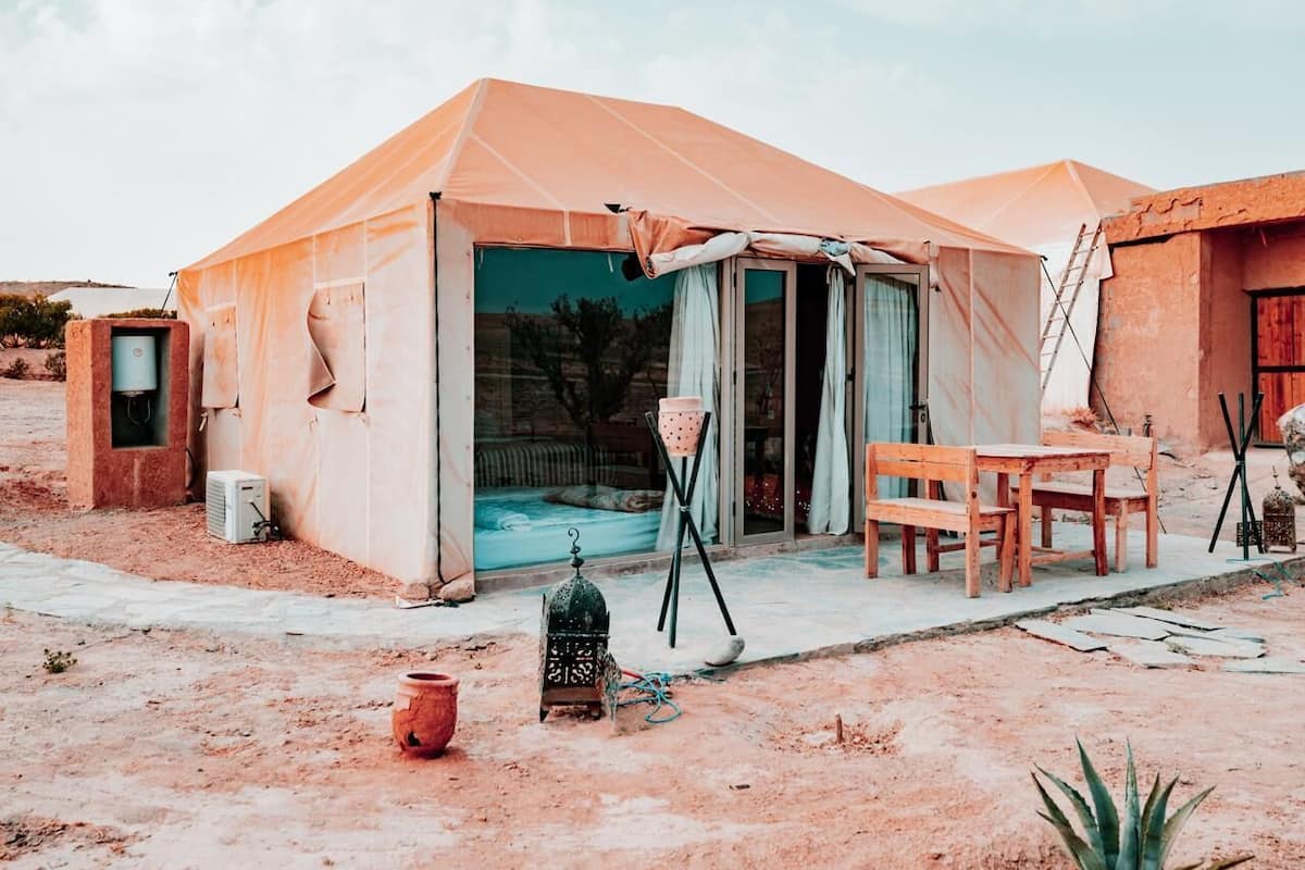 A tent with a sliding door, a small table, a chair, and a birdcage outside.