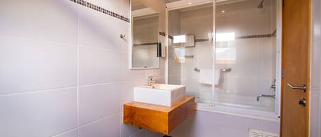 Un baño moderno con tocador de madera, un espejo grande y ducha con mampara de vidrio.
