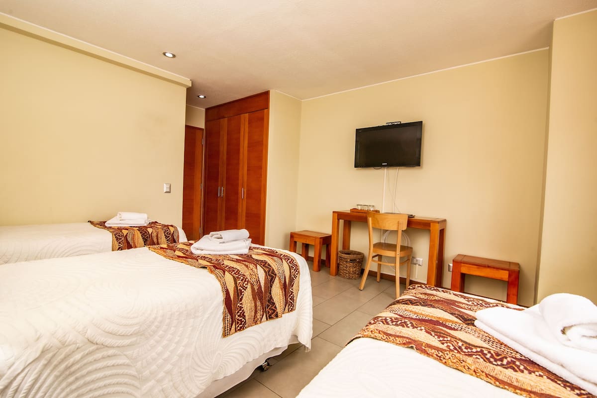 A hotel room with two beds, a desk, a chair, a television, and a wooden wardrobe.