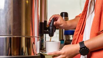Eine Person bedient eine Kaffeemaschine und hält eine Tasse unter dem Auslauf.