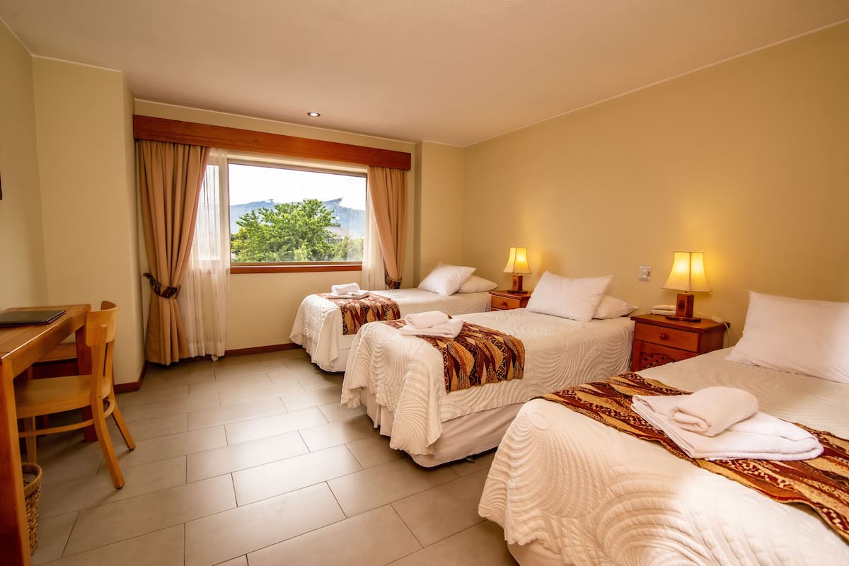 A hotel room with three beds, a desk, and a window with curtains.