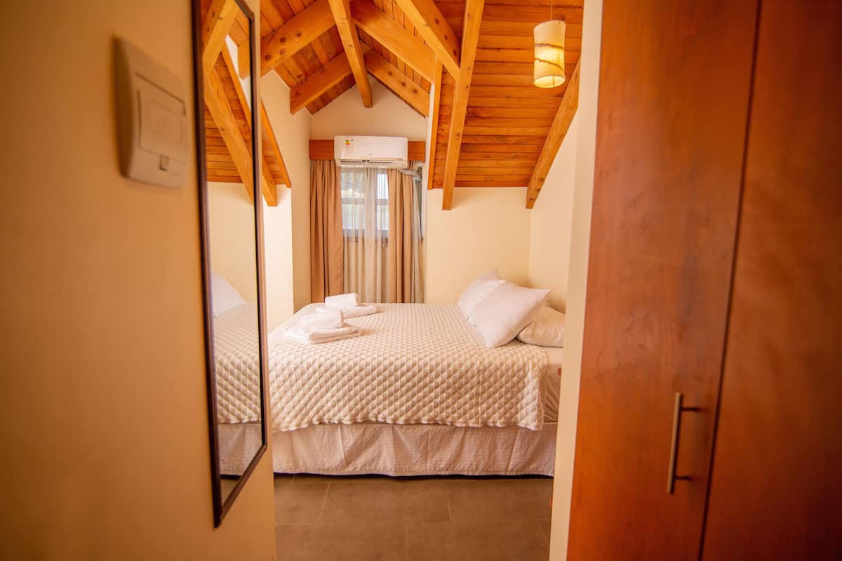 A bedroom with a wooden ceiling, a bed with white bedding, and a window with curtains.