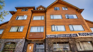 A multi-story hotel with wooden facade and stone accents, featuring a sign that reads "Hotel Vientos del Sur."
