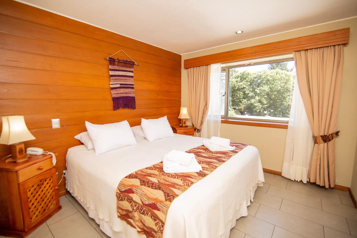 A hotel room with a large bed, wooden walls, a window with curtains, and a hanging tapestry.