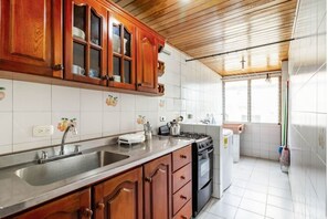Een keuken met houten kastjes, een roestvrijstalen spoelbak, een fornuis en een koelkast.